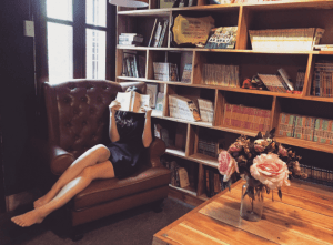 woman reading in large armchair next to bookshelf