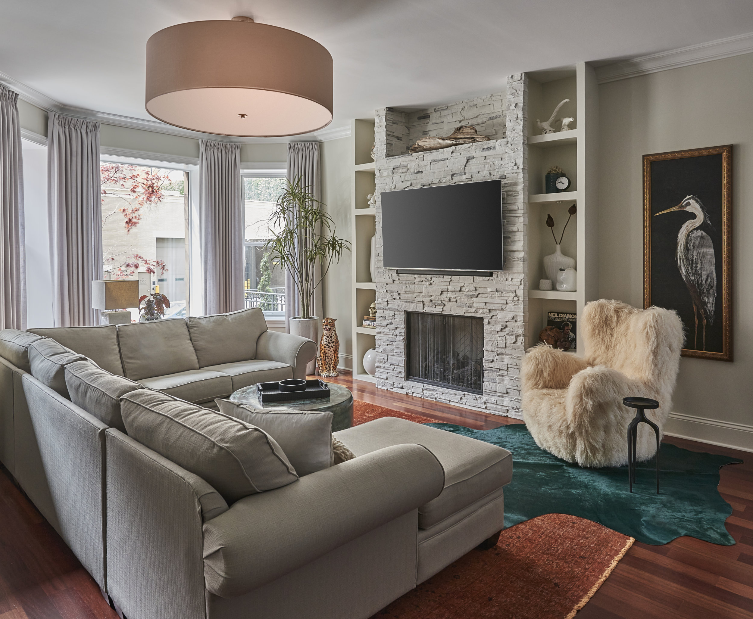 Example of a large 1960s formal and open concept medium tone wood floor and brown floor living room design in Chicago with beige walls, a standard fireplace, a stone fireplace and a wall-mounted tv